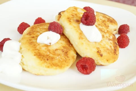 Golden syrnyky stacked on a plate, dusted with sugar and served with sour cream