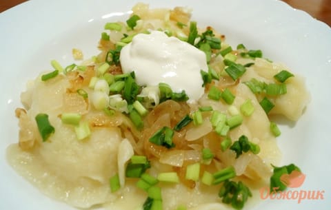 A plate of potato varenyky topped with golden fried onion, spring onion and sour cream