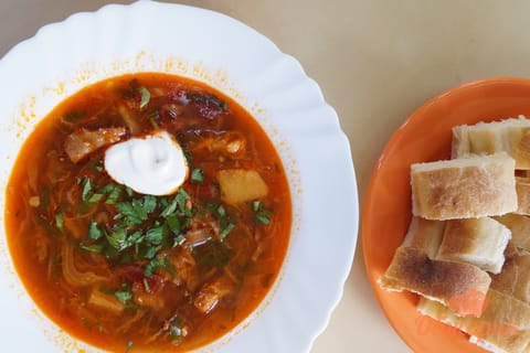 A bowl of deep red Ukrainian borscht with a spoonful of sour cream and chopped dill