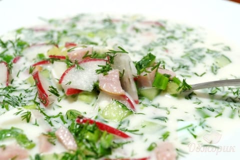 A bowl of cold okroshka with diced radish, cucumber, egg and herbs